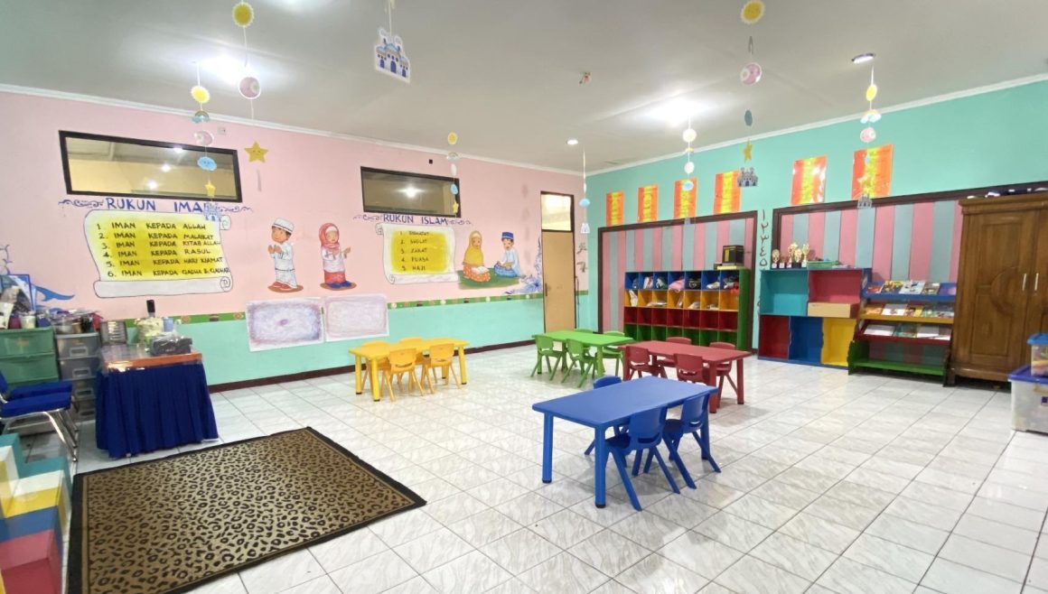Ruang kelas berdinding merah muda dengan meja dan kursi kecil warna-warni