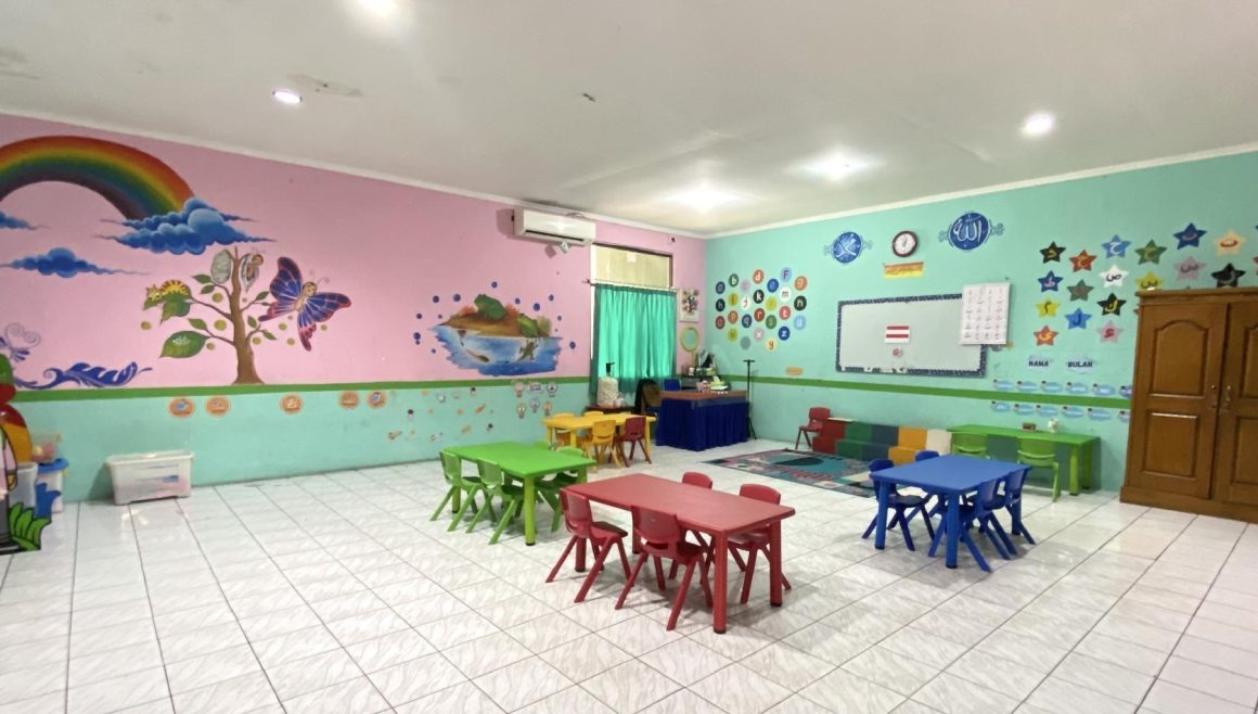 Ruang kelas bermural pelangi dengan meja dan kursi kecil warna-warni