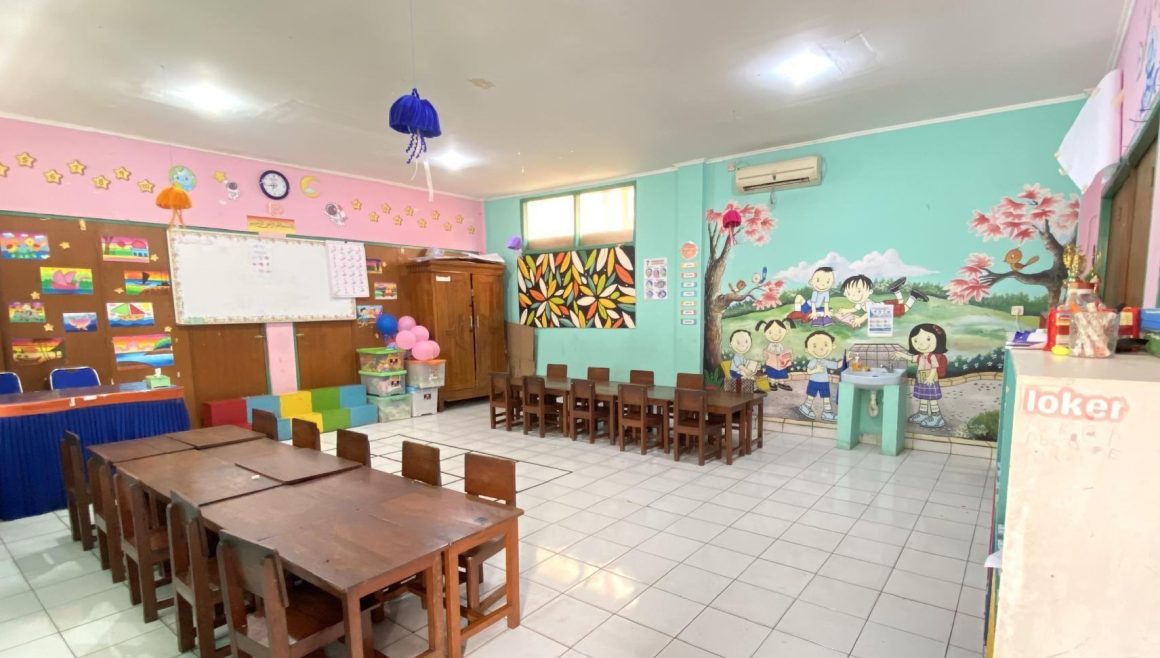 Ruang kelas dengan meja kayu panjang dan mural di dinding