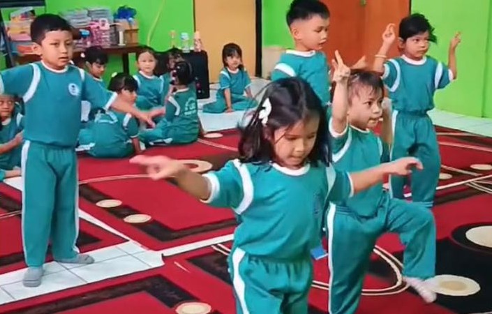 Anak-anak berseragam olahraga menirukan gerakan tari di kelas