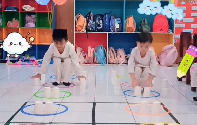 Dua anak menyusun gelas kertas di dalam lingkaran warna-warni di lantai kelas